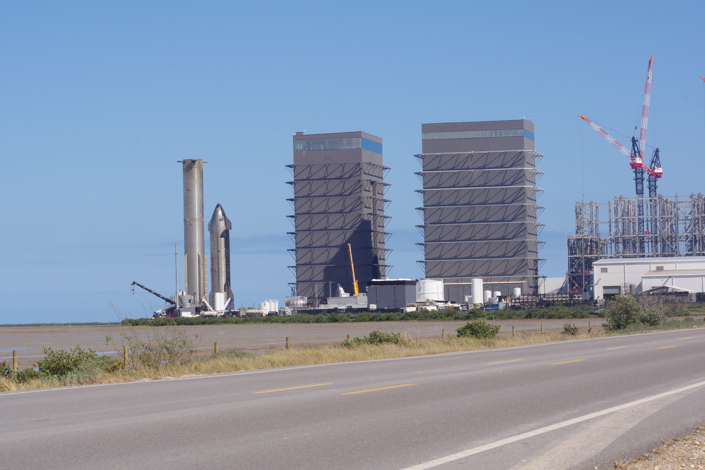 Wide view of Starbase from the road showing Super Heavy, Starship, High Bays and cranes
