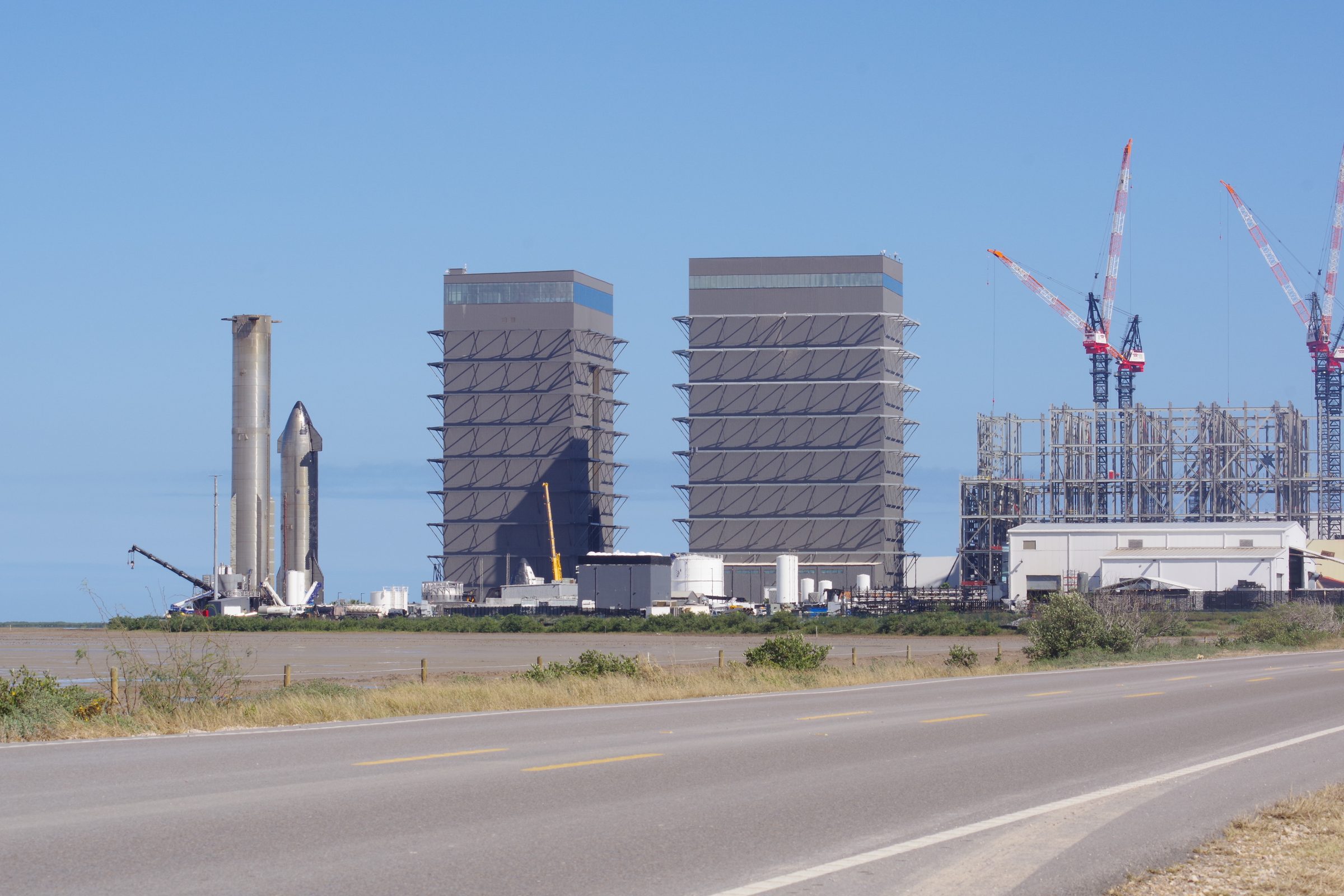 Super Heavy and Starship with twin High Bays, construction frame and cranes, road in the foreground